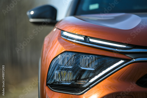 Front headlights and hood of orange modern prestigious car on nature background. Close up.