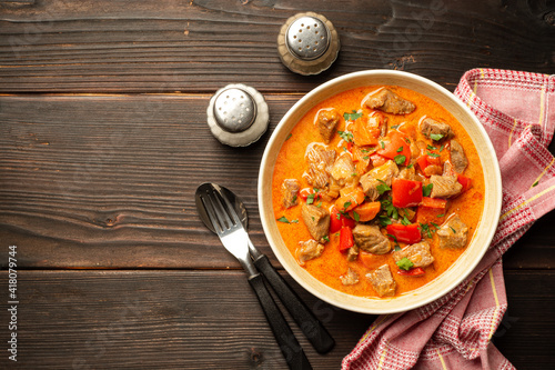 Traditional hungarian paprikash with turkey, bell pepper, carrot, onion, paprika and sour cream in bowl on dark wooden background