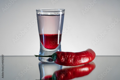 Single, reflected mad dog shot drink with tabasco sauce, raspberry syrup and chilli on side with smooth background