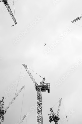 Czarno-białe centralne ujęcie samolotu na tle szarego nieba z sylwetkami dźwigów 