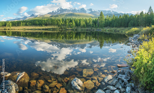 Picturesque mountain lake in the summer morning, Altai. Beautiful reflection of mountains, sky and white clouds. Clear water, stones at the bottom.