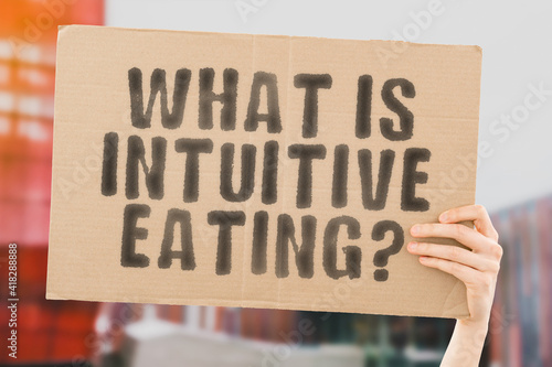 The question " What is intuitive eating? " on a banner in hand with blurred background. Food. Meal. Nutrition. Healthcare. Nutrient. Brain. Mind. Freedom. Free. Choice