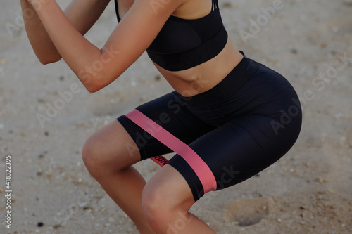 beautiful sports girl is engaged in fitness with rubber bands by the sea
