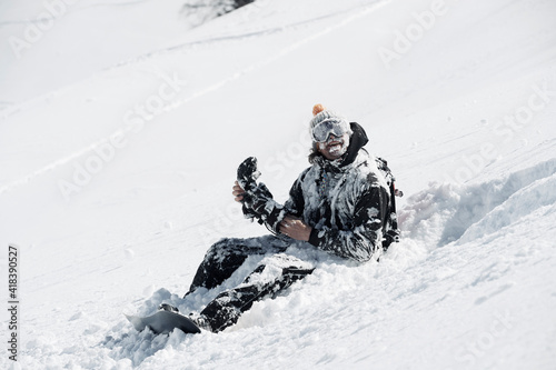 Male snowboarder covered in snow sitting on mountainside, Alpe-d'Huez, Rhone-Alpes, France