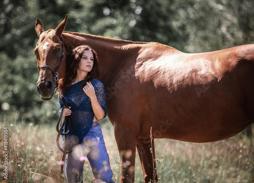 A beautiful curly-haired girl stands next to a red horse