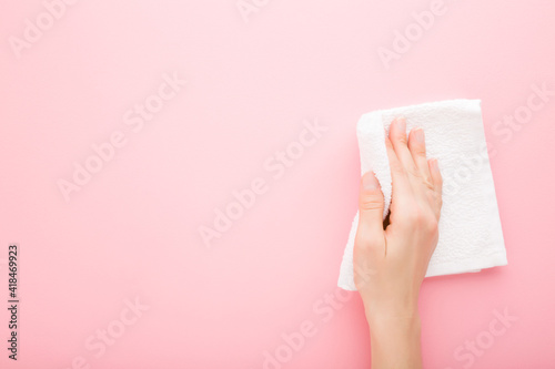 Young adult woman hand holding white rag and wiping table, wall or floor surface in kitchen, bathroom or other room. Empty place for text or logo. Light pink background. Pastel color. Top down view.