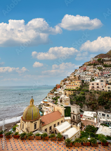 View of a seaside village with many colorful stone houses and residential buildings along the Amalfi Coast in Italy with a partially blue sky and scattered clouds.