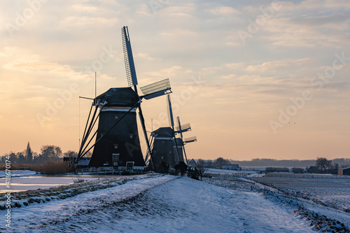 The three windmills in a row during sunrise on a cold winter morning with a snowy landscape at the three windmills in Leidschendam, The Netherlands