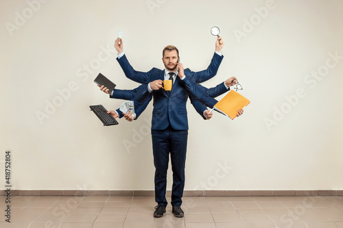 Businessman with many hands in a suit. Works simultaneously with several objects, a mug, a magnifying glass, papers, a contract, a telephone. Multitasking, efficient business worker concept.