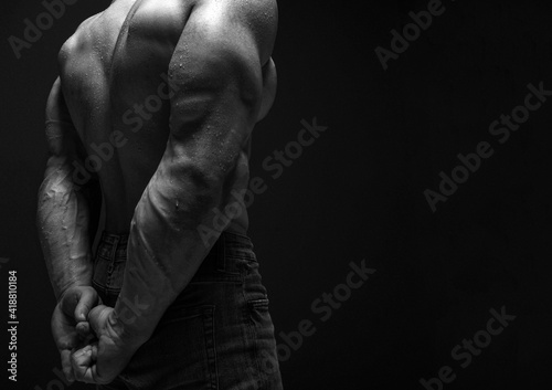 Pumped up strong sweaty upper body back and biceps of brutal man athlete in jeans standing showing perfect shape over dark background. Sport men body concept