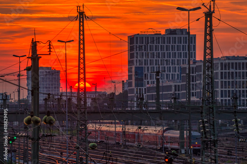 Impressive sunset over Munich and a business district in the background with the view over a railway with a driving train at the late evening.