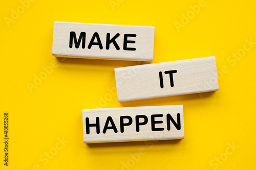 MAKE IT HAPPEN . Saying. expression written on a wooden bars on a yellow background