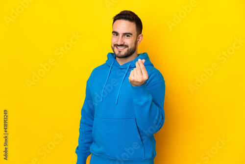 Young caucasian handsome man isolated on yellow background making money gesture