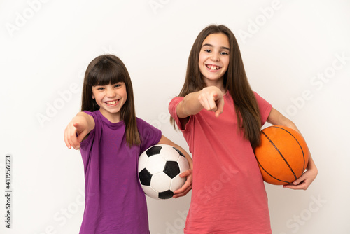 Little sisters playing football and basketball isolated on white background points finger at you with a confident expression