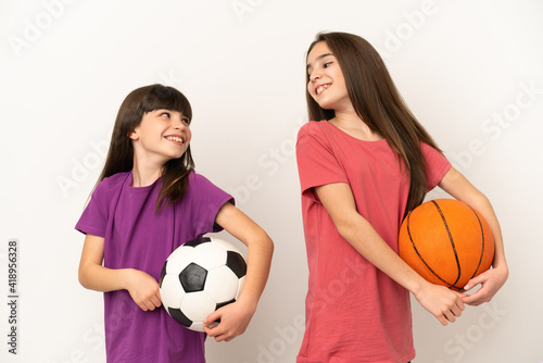 Little sisters playing football and basketball isolated on white background looking over the shoulder with a smile