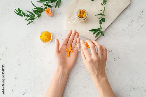 Female hands with turmeric pills, powder and roots on light background