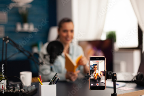 Vlogger holding book during podcast review on social media. Creative content creator influencer streaming live video, recording digital social media communication for her audience