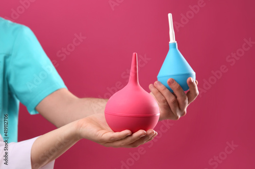 People holding enemas on pink background, closeup