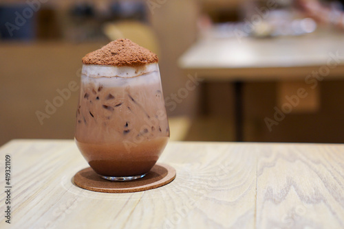 Iced Chocolate Bomb topped with cocoa powder likes volcano on wooden table in cafe.