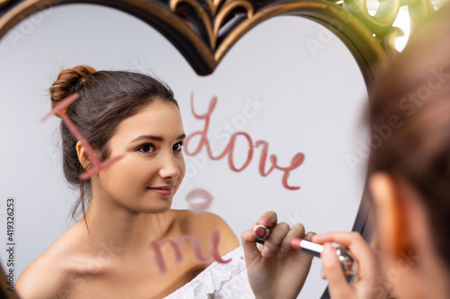 Portrait of a beautiful caucasian girl looking in the mirror and writing I love me near a heart, self-love