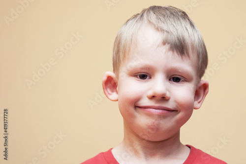 Portrait of smiling boy with brown eyes in red outfit posing for camera on beige background in studio close view
