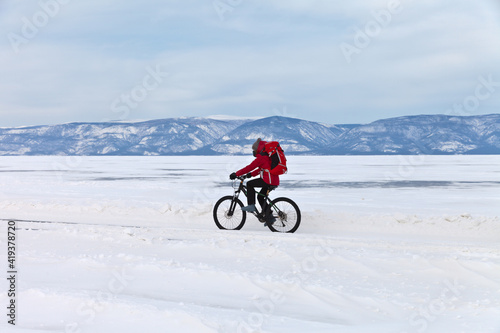 Winter Baikal Lake. A tourist girl travels on a bicycle on the ice of the frozen Small Sea along Olkhon Island. Healthy lifestyle. Ice travel and outdoor activities