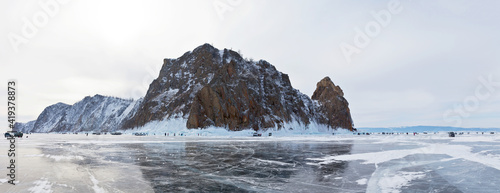 Frozen Lake Baikal. Groups of tourists arrive by car across the ice of lake to Cape Hoboy, the tip of Olkhon Island. Panoramic view from ice to the famous Deva Rock. Winter travel. Natural background
