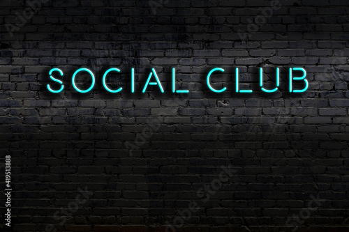 Neon sign. Word social club against brick wall. Night view