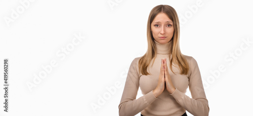 Attractive blond girl prays for wellness of family, keeps palms pressed together in praying gesture. Copy space