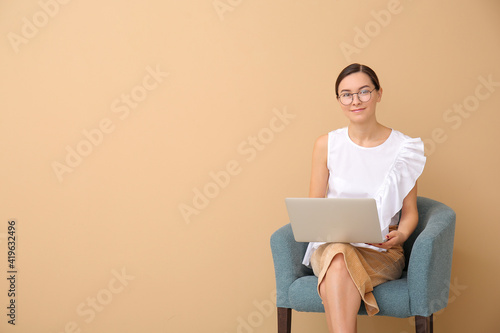 Portrait of female psychologist sitting in armchair against color background