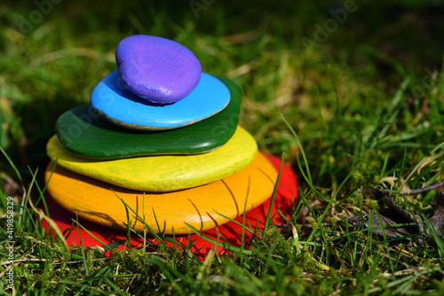Several brightly colored pebbles painted in rainbow colors lie on top of one another in a meadow with green grass