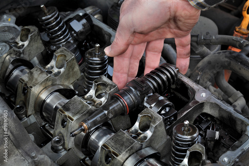 Car mechanic fixing modern diesel engine, closeup of hand removing injectors from cylinder head