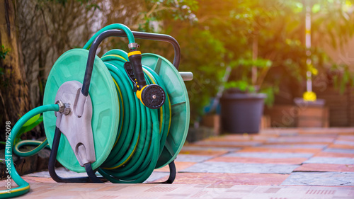 The old water hose roll up with nozzle on tile floor in home gardening area