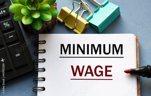 MINIMUM WAGE - word is written in a notebook with a marker, calculator, clamps and cactus