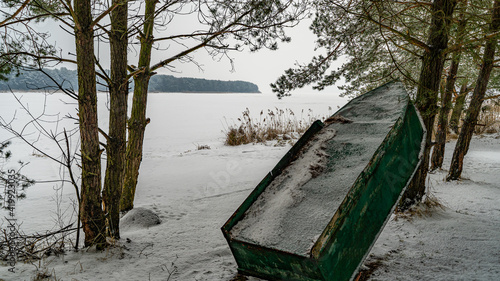 Łódka oparta o drzewo, jezioro skute lodem, śnieg