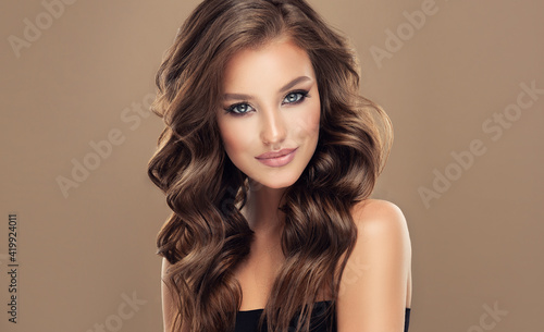 Beautiful model girl with long wavy and shiny hair . Brunette woman with curly hairstyle 