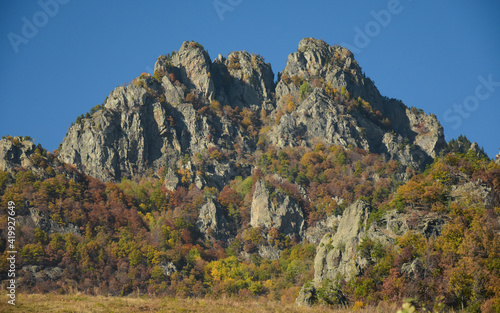 The eroded calcareous cliff of Cozia Mountains raising above a pasture. Autumn season, the beech forest got colored leaves. Carpathia, Romania 