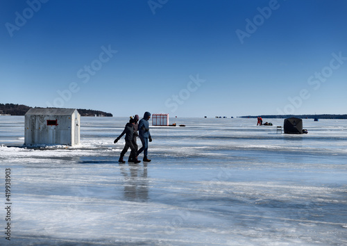 Blue ice and sky at Kempenfelt Bay of Lake Simcoe with ice fishing shacks and people walking on ice Barrie Canada