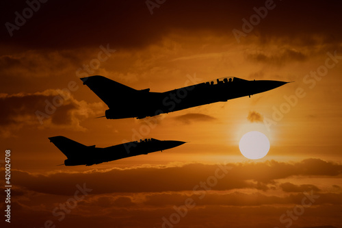 Fighter jets silhouettes at sunset, interceptor military aircraft on a combat mission to intercept foreign aeroplanes. 