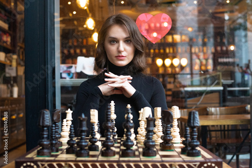 Beautiful girl play chess, queen’s gambit play and everyone wins, smart and pensive face. White and black chess pieces are displayed on the board. Mental game, lot of time to last, not for fools.