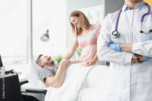 Happy man lies on hospital bed his hand is held by woman next to doctor