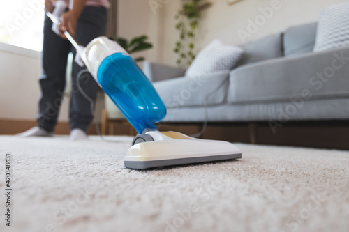 Close up on vacuum cleaner while woman cleaning the carpet in the living room. Asian woman doing chores at home.