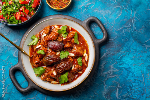 Traditional Moroccan lamb tagine simmered in spices, with dates and almonds. Salad and spices. Blue background.