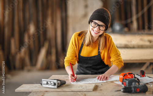 Smiling craftswoman working with l papers in joinery workshop