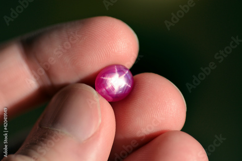 Natural 6 rays star loose red ruby oval cabochon gemstone holded in hand fingers on bright sunny day light. Heated lead glass filled ruby gem. Precious gemstone, corundum Al2O3 Aluminium oxide formula