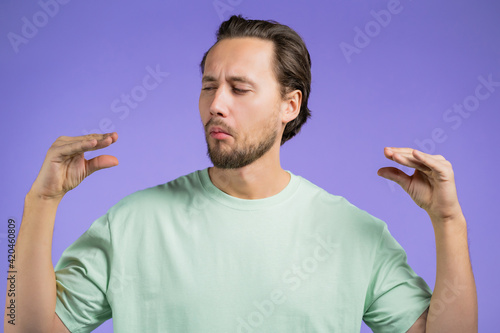 Handsome bored man showing bla-bla-bla gesture with hands and rolling eyes isolated on violet background. Empty promises, blah concept. Lier