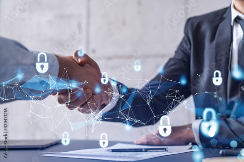 Handshake of two businessmen who enters into the contract to protect cyber security of international company. Padlock Hologram icons over the table with documents.