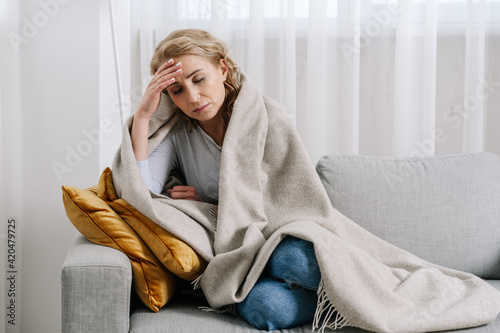 Ill woman covered with blanket sit on sofa