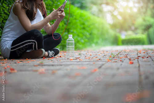 Close up of water bottle. Woman sitting on the smartphone after exercise in the park.