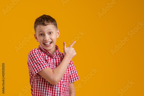 cheerful, happy child points up, copying the place for the text. A smiling, enthusiastic teenage boy in a plaid shirt shows off. Advertising concept.